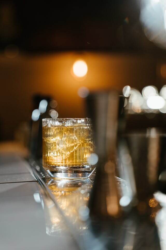 Glass of whiskey with ice cubes on a bar counter with warm ambient lighting.