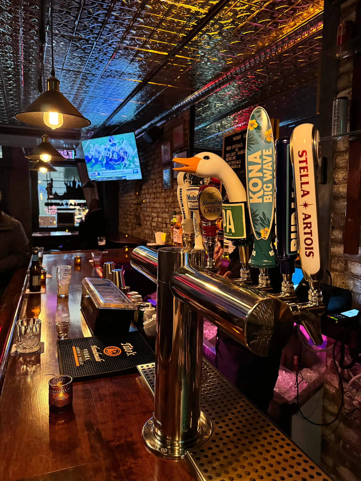 A bar counter with beer taps including a duck-shaped tap handle, and illuminated hanging lamps above.