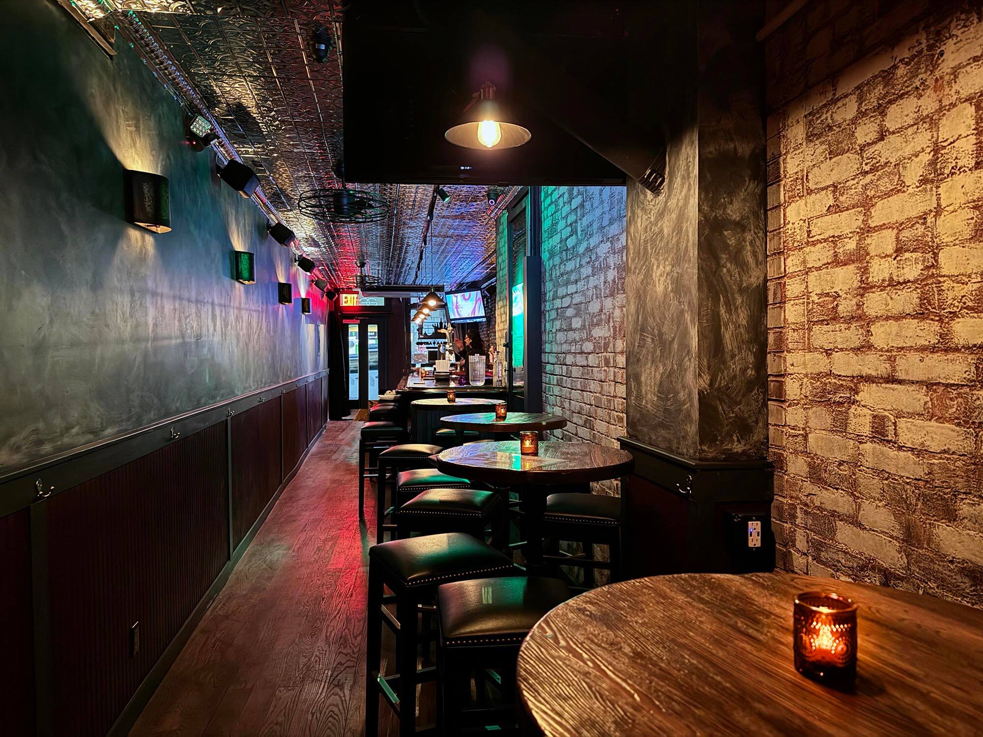 Cozy bar interior with wooden tables, stools, exposed brick walls, and warm ambient lighting.