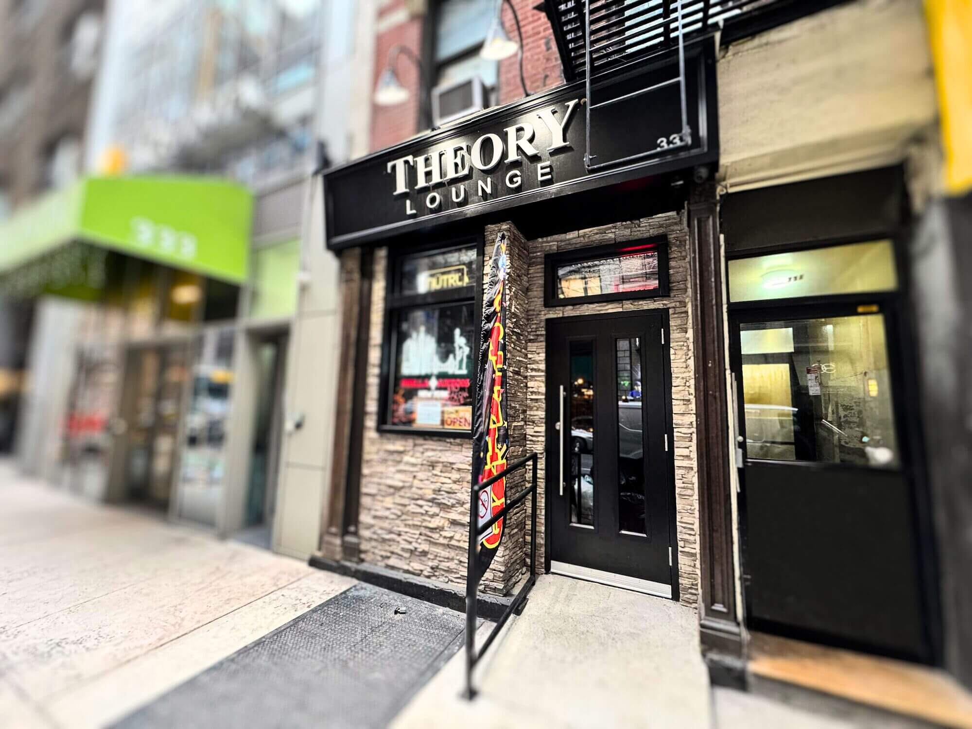 Entrance to Theory Lounge with black double doors and stone facade on a city street.